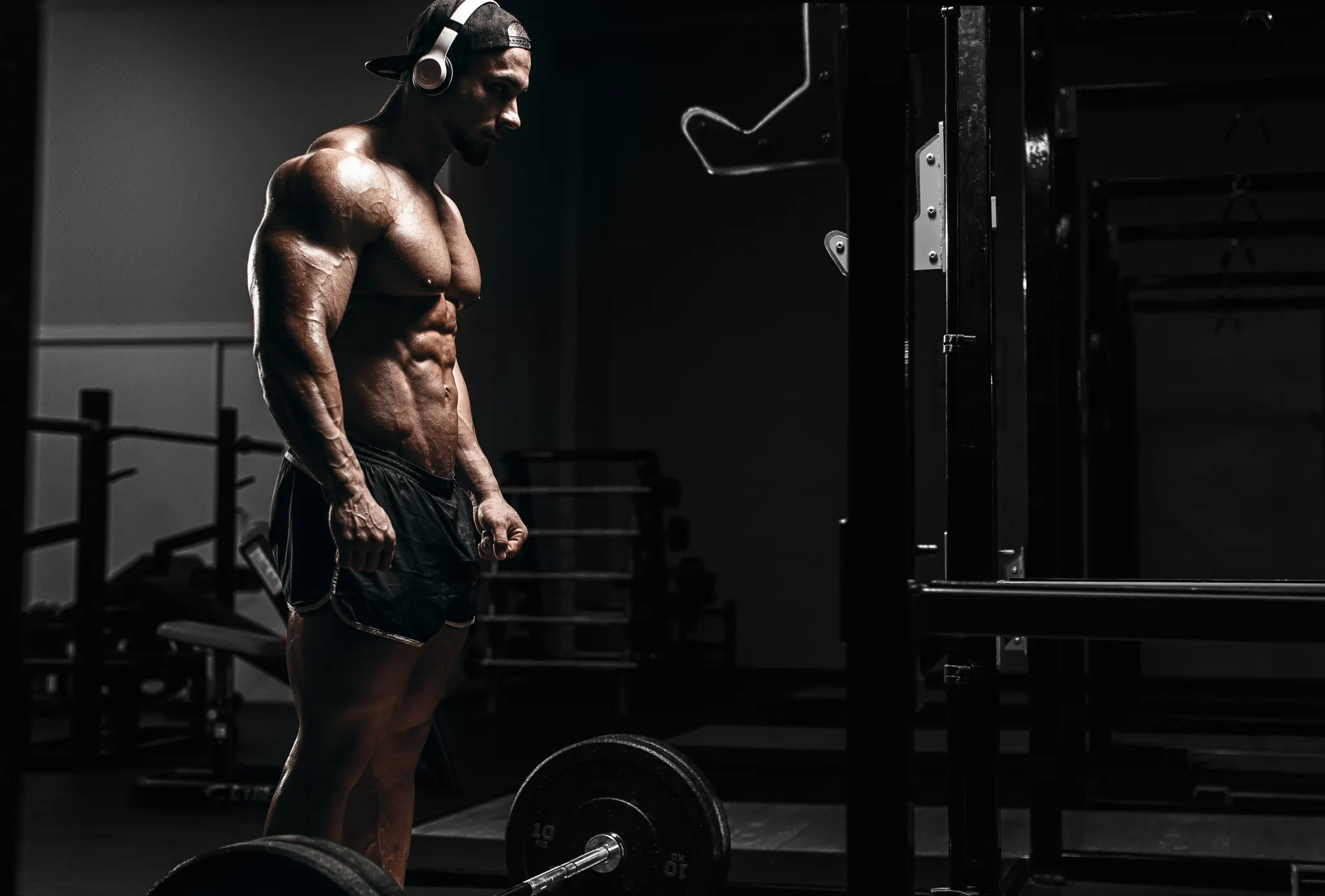Shirtless muscular man with headphones in a dark gym — the ideal candidate